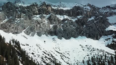 wide panorama flight at a glacier rock snow mountain top near bavaria elmau castle in the bavarian austrian alps on a cloudy and sunny day along trees and forest in nature with avalanches going down