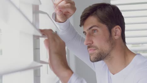 Man-looking-through-window-blind-at-home-4k