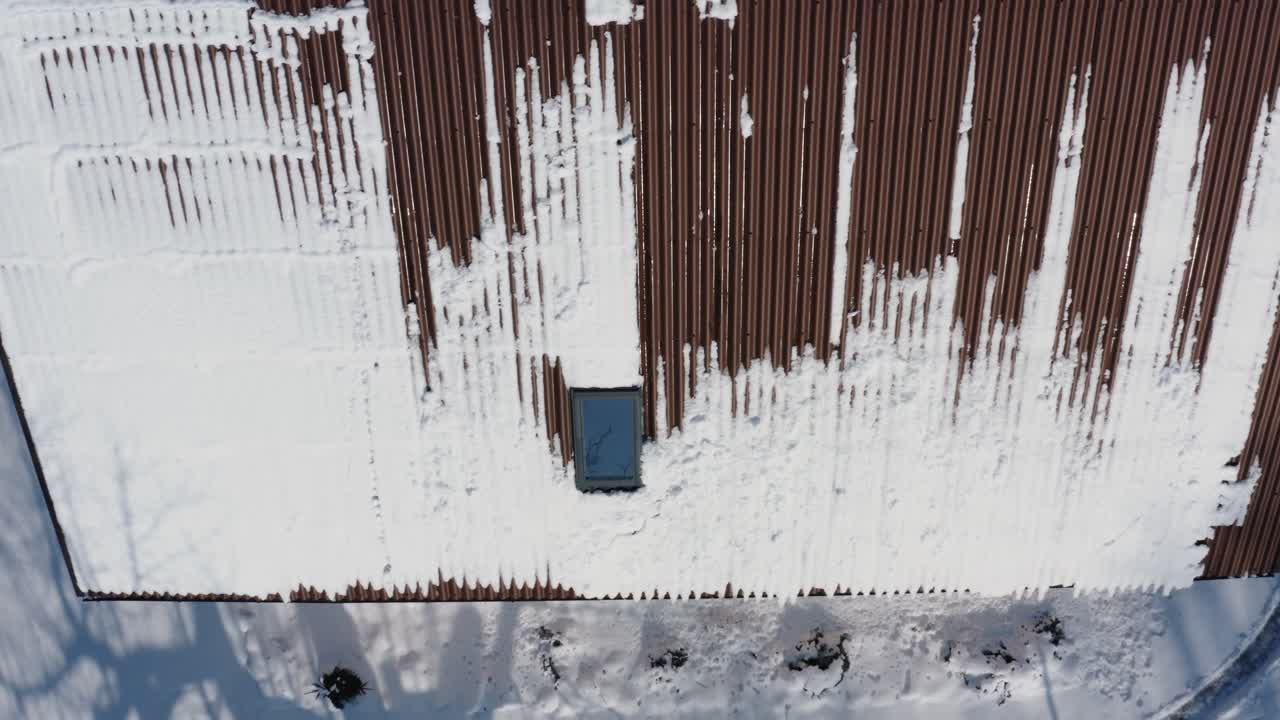 Flying above a roof covered in snow. Snow melting on a roof in a sunny winter day. Aerial drone view of a brown house roof.