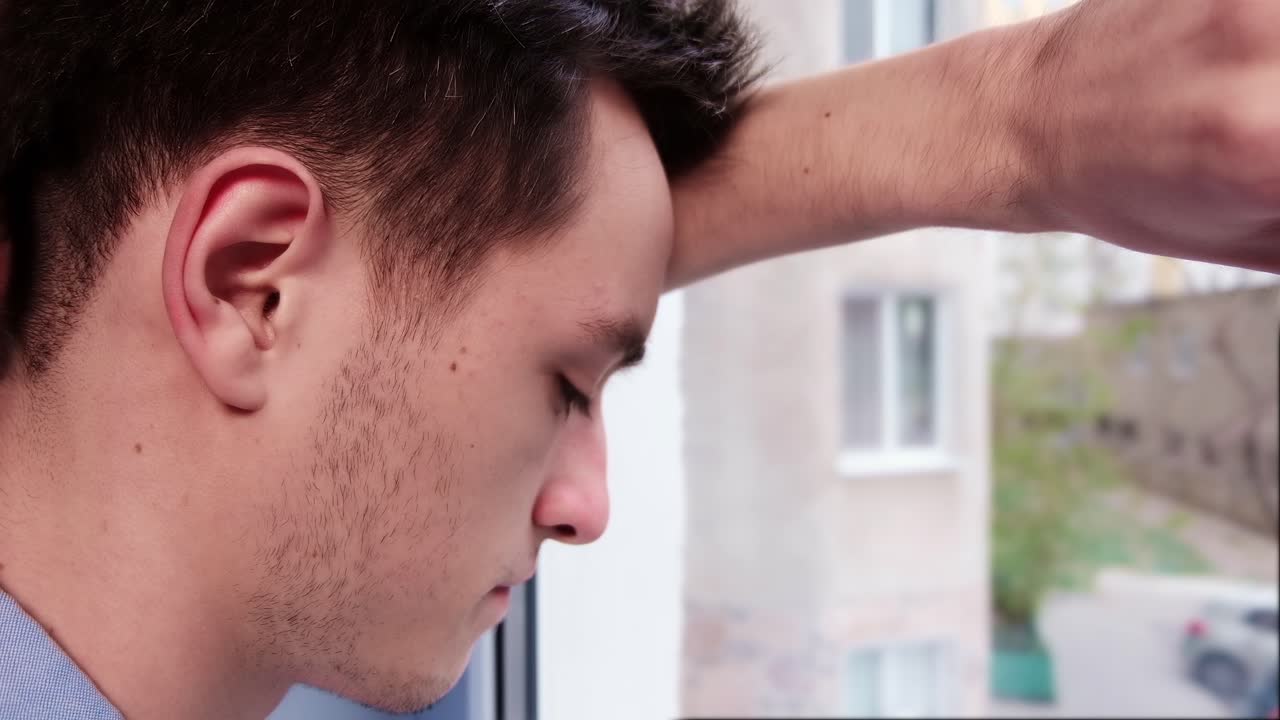 Bored man in blue shirt looking desperate out of the window. Close up. Quarantine and Corona Virus idea