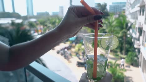 girl-holds-half-empty-glass-with-mojito-cocktail-on-balcony