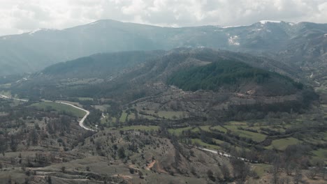 A-drone-shot-of-forest-mountains-with-snow,-warm-weather,-little-village,-flying-above-a-dreamy-hill,-4K-video,-European-winter-nature,-scenic-white-clouds,-beautiful-landscape