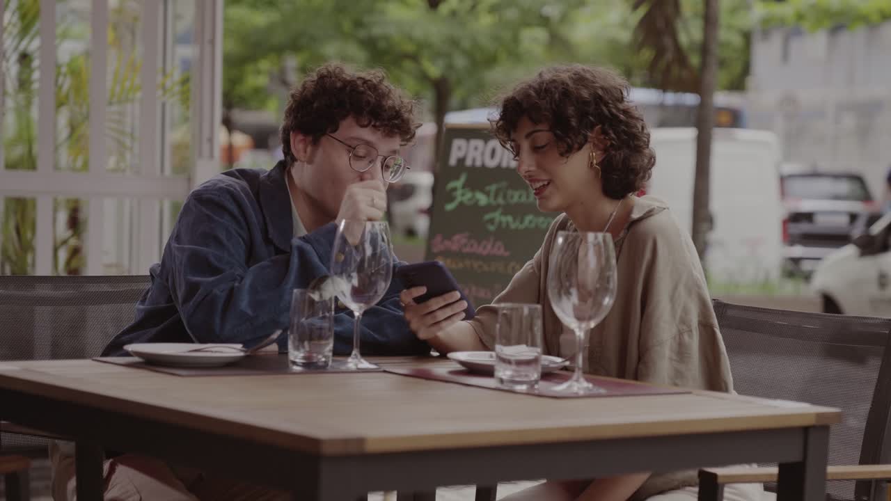 Two young adults share a moment looking at a smartphone at an outdoor cafe