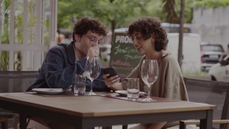 two young adults share a moment looking at a smartphone at an outdoor cafe