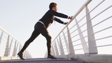 African-american-man-stretching,-leaning-on-footbridge-exercising-outdoors