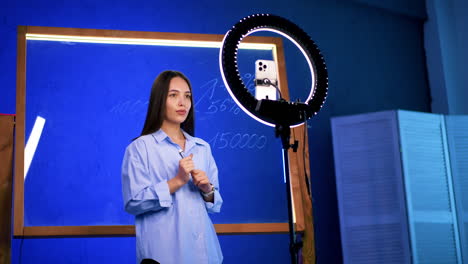 young teacher in modern class. a young woman stands in front of a chalkboard, explaining a lesson while using a ring light to engage with her audience