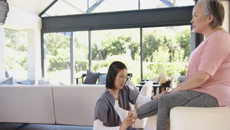 physiotherapist assisting senior asian woman with leg exercises in bright living room