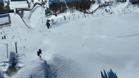 high altitude shot of bottom of ski run, static shot of skiers arriving at base of mountain lining up for the chairlifts