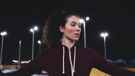 Sportive-Curly-Girl-Stretching-And-Rotating-Arms-In-The-Park-At-Night-2