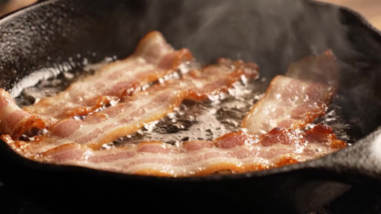 Fette croccanti di pancetta che friggono in una padella di ghisa, catturando il suono sfrigolante e l'aroma irresistibile di prelibatezze per la colazione cucinate alla perfezione