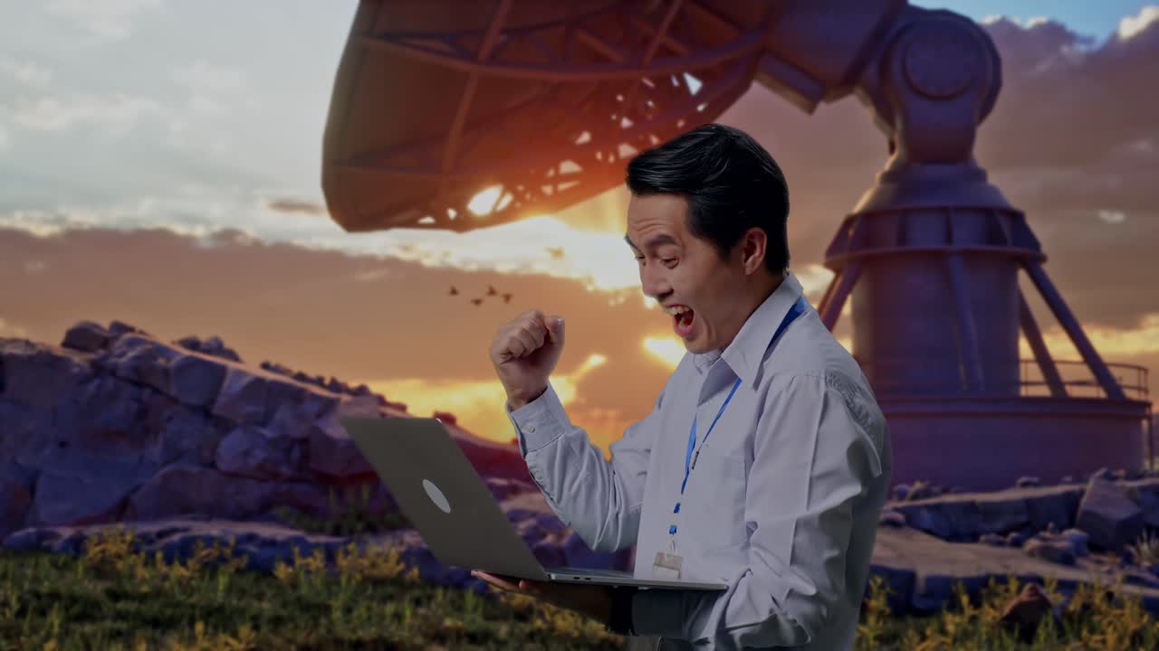 Side View Of An Asian Male Professional Worker Standing With His Laptop With Large Satellite Dish, He Raises His Fist Up With Screaming Goal After Typed On The Laptop