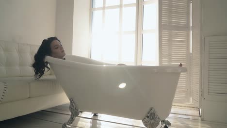 girl-with-curly-hair-lies-in-stylish-bath-at-bright-sunlight