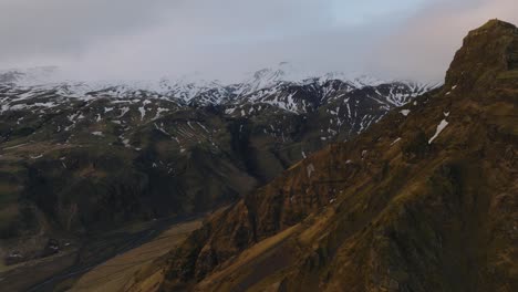 Aerial-landscape-view-of-a-river-flowing-in-a-mountain-valley,-coming-down-from-melting-snow,-in-Iceland,-on-a-moody-day