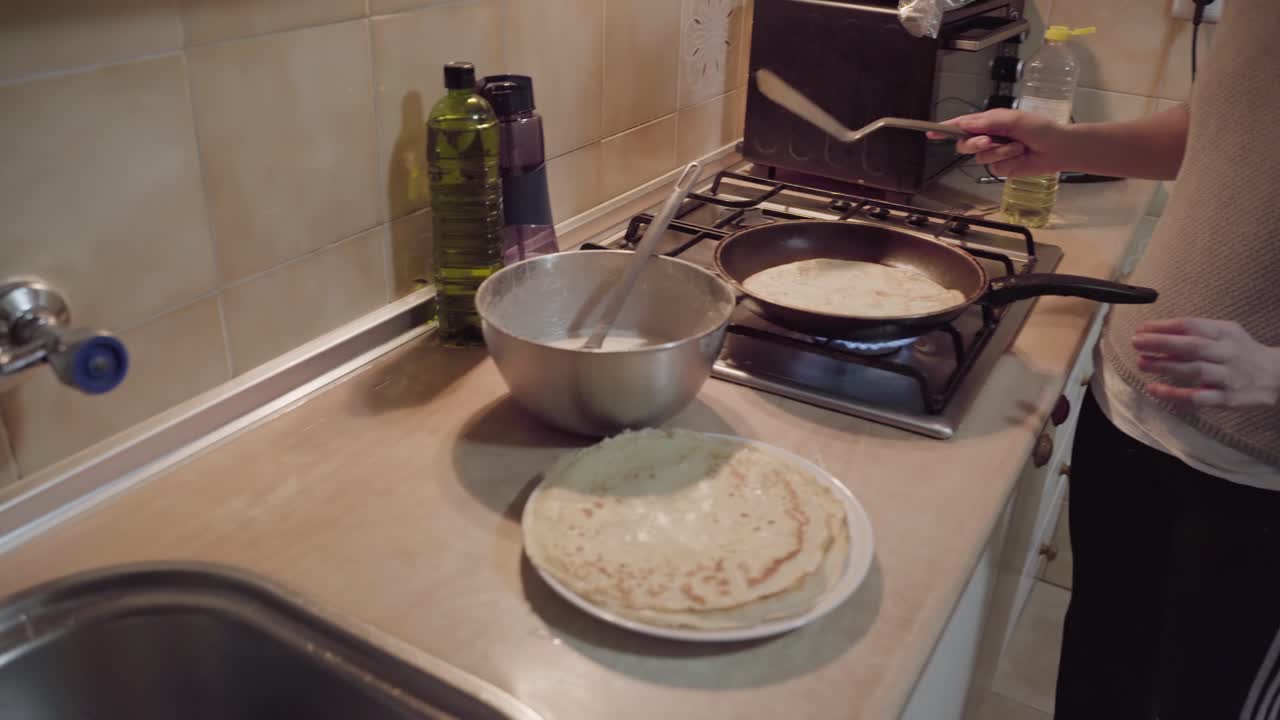 여자가 부엌에서 오른쪽으로 패닝하는 스토브에 있는 팬케이크를 다른 쪽으로 돌리고 있습니다.
