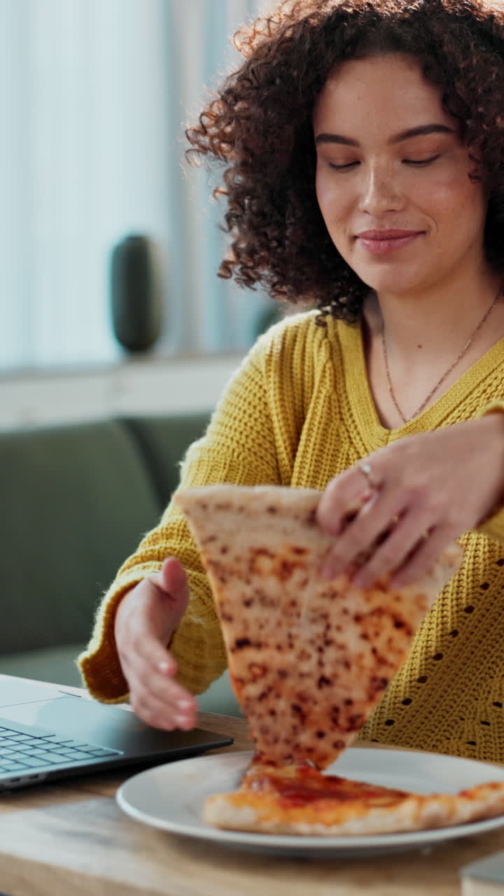 Jovem mulher comendo pizza enquanto trabalha no laptop em casa