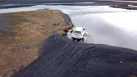 4WD-white-rental-SUV-crossing-a-glacial-river-in-deep-water-on-volcanic-sand-and-rock-aerial-trucking-shot