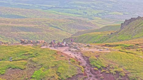 aerial view over green hill at b-29 crash site in high peak, england, as hikers gather around stone memorial.