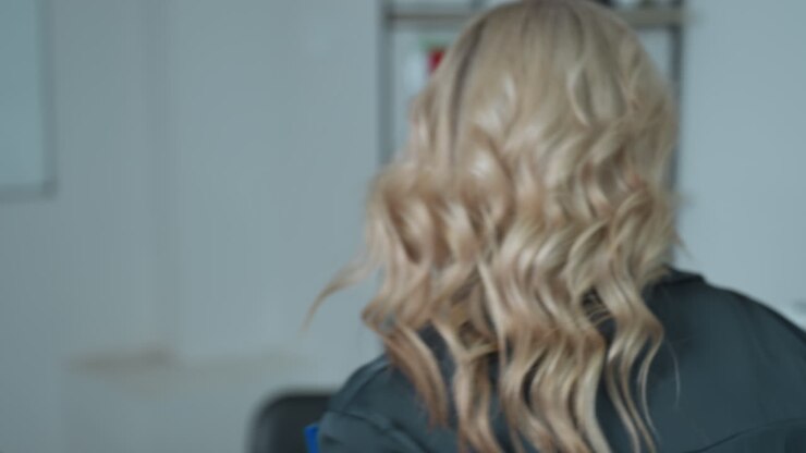 Confident woman in black top walks toward desk carrying file, preparing to begin workday in clean office space, with soft lighting and professional demeanor reflecting calm focus
