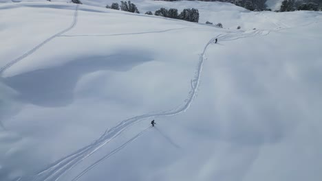 aerial following young sports group skiing down snow covered glacier mountain range slope in snowy alpine scenery, top down view