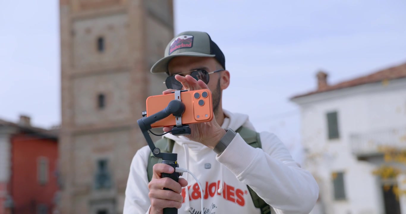 บุคคลกำลังถือกล้อง DJI Osmo Mobile Gimbal ซึ่งแสดงอุปกรณ์ถ่ายทำภาพยนตร์แบบมือถือ ภาพระยะใกล้