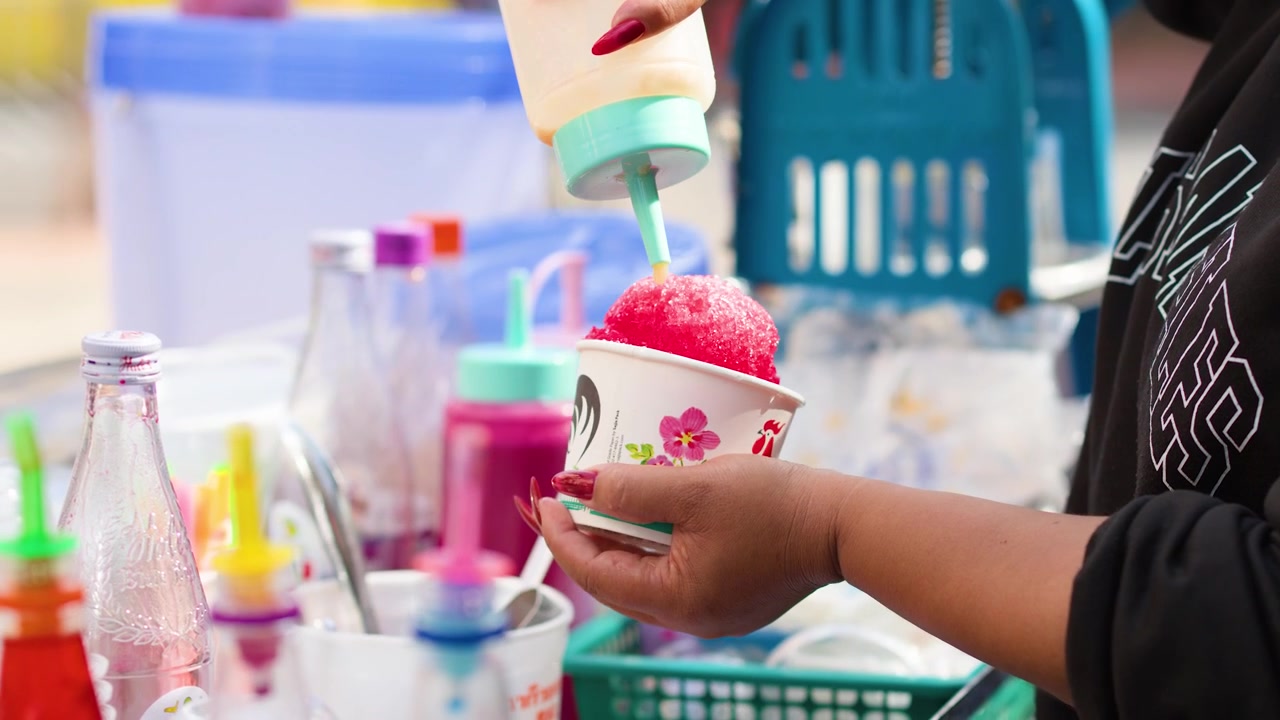 Un venditore prepara una granita colorata in un mercato all'aperto a Bangkok, Thailandia.