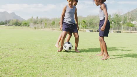 video of three happy african american schoolchildren playing football barefoot in field