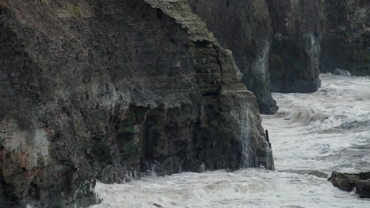 Powerful waves breaking hard at high tide against Jurassic cliffs in slow motion, North East England, UK.