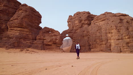 Man-Walking-Near-Elephant-Shaped-Rock-At-Sunset-In-Tassili-N'Ajjer-National-Park,-Algeria---Drone-Shot