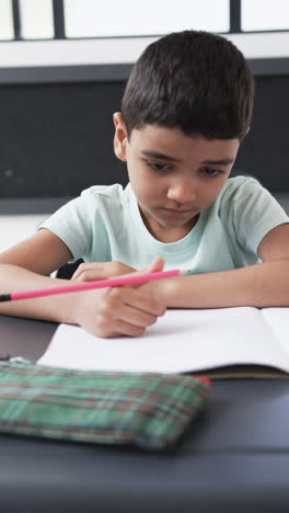 vertical video: in a school setting, a young caucasian boy focuses on writing