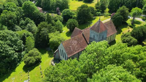 a slow arc-shot of st lawrence the martyr church, with trees blowing in the wind in the foreground, and with the cemetery in view