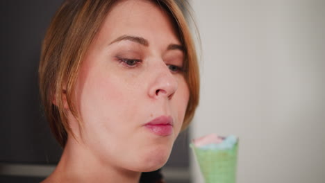 close up of lady savoring colorful ice cream with green cone, traces of dessert on lips as she enjoys sweet treat standing indoors, showing satisfaction and indulgence in bright modern space