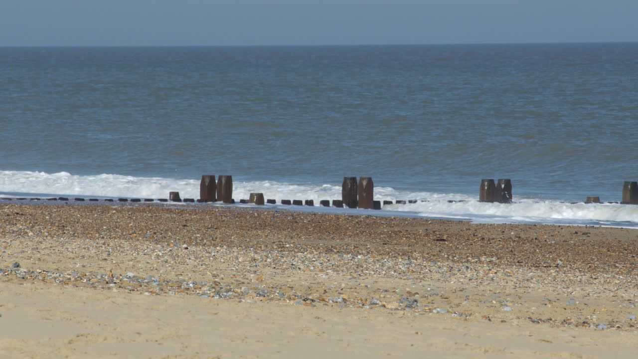 Wide shot of the waves crashing over the sea defence groynes at Walcott Beach