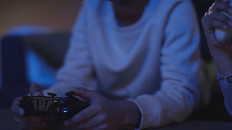 Primo piano di due giovani ragazzi a casa che giocano con una console di videogiochi in TV tenendo i controller a tarda notte 4
