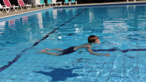a young boy swimming in a blue pool on a sunny day