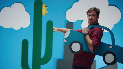 man with cardboard car in front of a paper scene