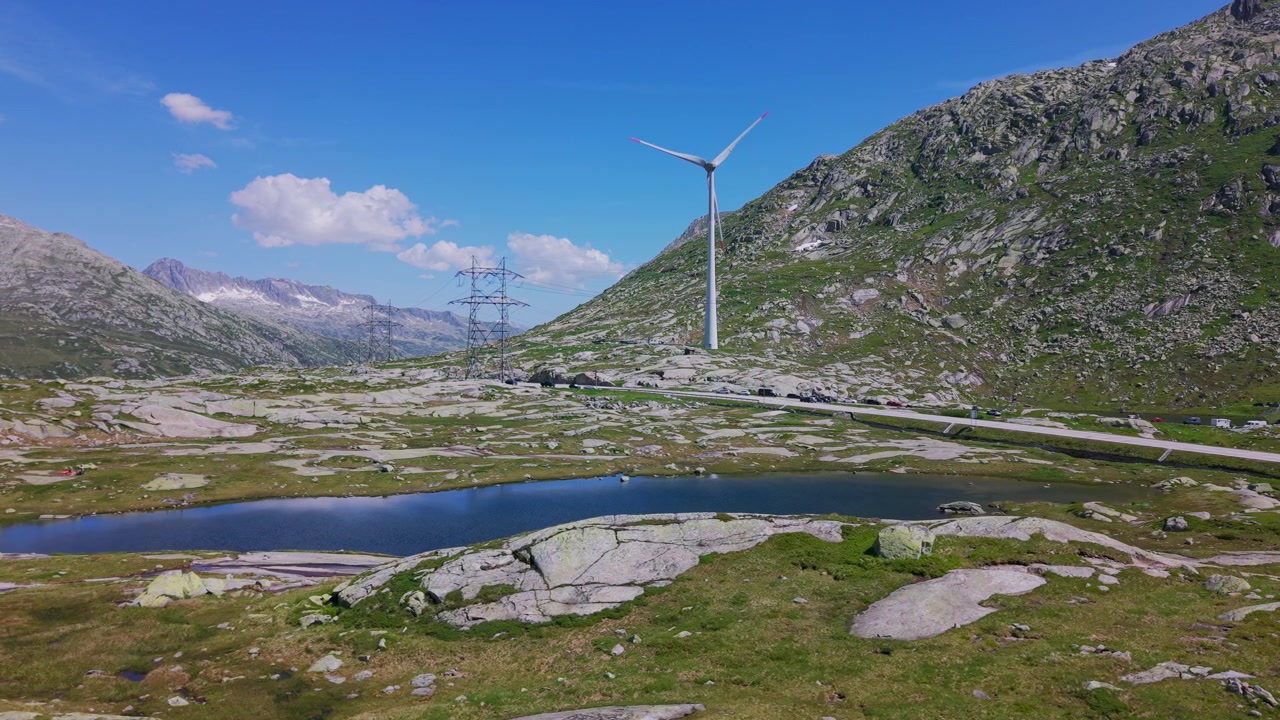 Turbina eolica e traliccio elettrico accanto a un lago di montagna su un passo alpino in Svizzera. Drone aereo che vola a bassa quota.