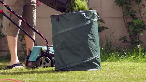 man throwing freshly cut grass from his backyard lawn into a green binder - slow motion