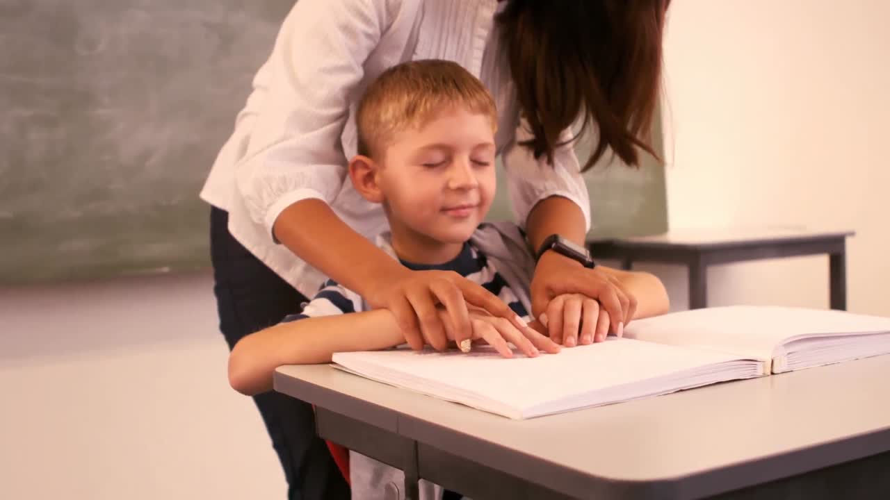 un maestro ayudando a un escolar ciego con su tarea en el aula
