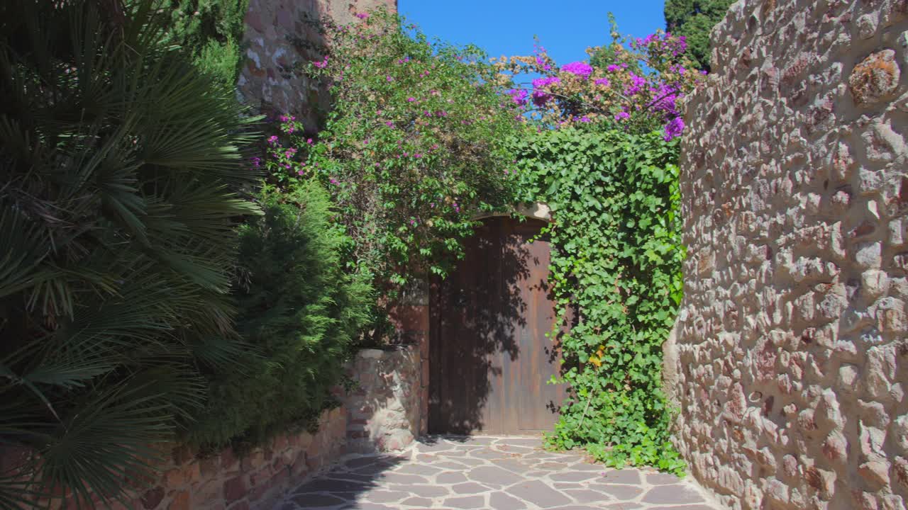 Via acciottolata in una città medievale con casa ricoperta di piante e fiori