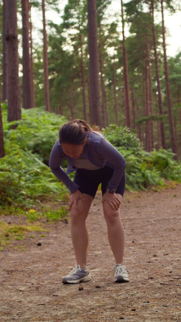 Video verticale di una donna che si allena all'aperto, correndo lungo un sentiero nel bosco e fermandosi per riprendere fiato, ripreso in tempo reale.
