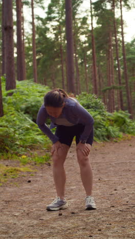 video vertical de una mujer haciendo ejercicio haciendo trabajo al aire libre corriendo a lo largo de una pista en el bosque deteniéndose para respirar disparado en tiempo real