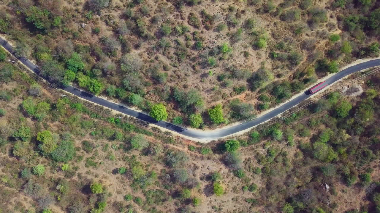 Aerial view of a bus passing through Ramanagara Road surrounded with wild bushes and trees in Karnataka, India.