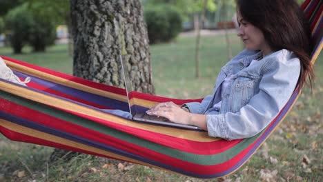 woman working on laptop in a hammock in a park