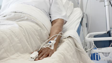 hand of african american senior female patient sleeping in bed in hospital room, slow motion