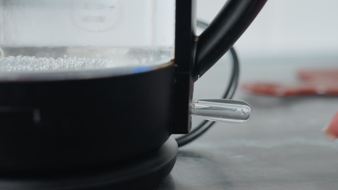 투명한 유리 비에서 거품이 상승하는 전기 물 보일러의 클로즈업, 물이 는 지점에 도달 할 때 증기가 형성되기 시작합니다, 온도 조절을위한 수동 조절 스위치