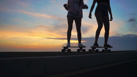 en medio de una cautivadora puesta de sol, dos amigos patinan en una carretera, enmarcada por montañas y un cielo pintoresco en cámara lenta. los pantalones cortos son su elección de ropa