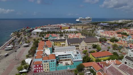 Toma-Aérea-Del-Centro-Histórico-De-Willemstad,-Curazao,-Con-Un-Crucero-Gigante-Al-Fondo