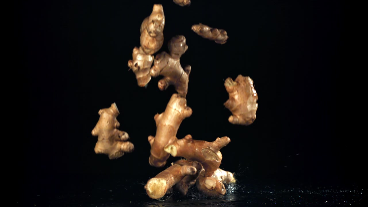 Fresh Ginger Roots Falling and Splashing on a Wet Black Surface