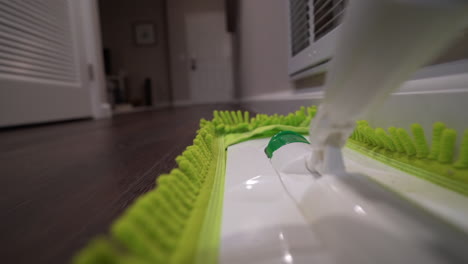 POV-slow-motion-of-dust-mop-cleaning-hardwood-floors-and-baseboard-in-apartment-hallway