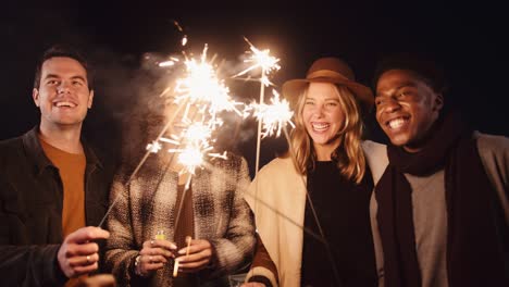 diverse group of friends laughing and lighting their sparklers outdoors in the night time. high quality 4k footage